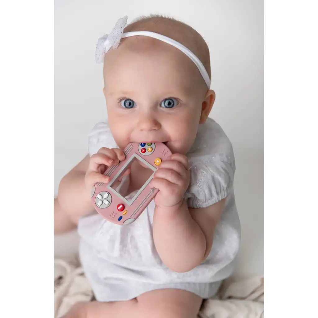 Cute pink video game inspired silicone teether being chewed on by a happy baby