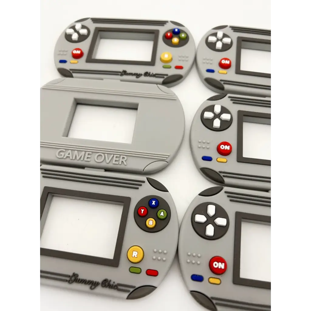 Gray video game inspired silicone teethers shaped like handheld gaming devices for babies