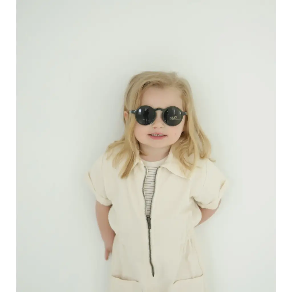 Young child rocking adorable round sunglasses and a cream outfit for summer fun