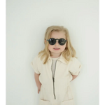 Young child rocking adorable round sunglasses and a cream outfit for summer fun