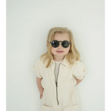 Young child rocking adorable round sunglasses and a cream outfit for summer fun