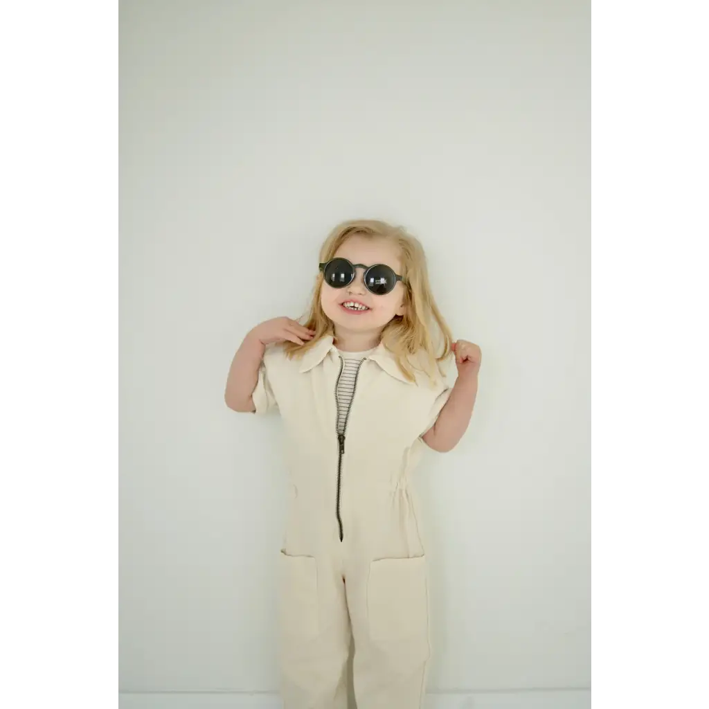 Person in a cream jumpsuit and dark sunglasses, showcasing adorable round sunglasses