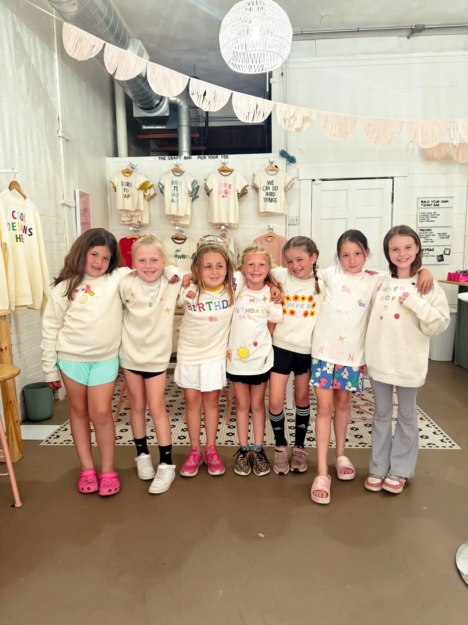 Seven young girls posing in matching cream-colored outfits.