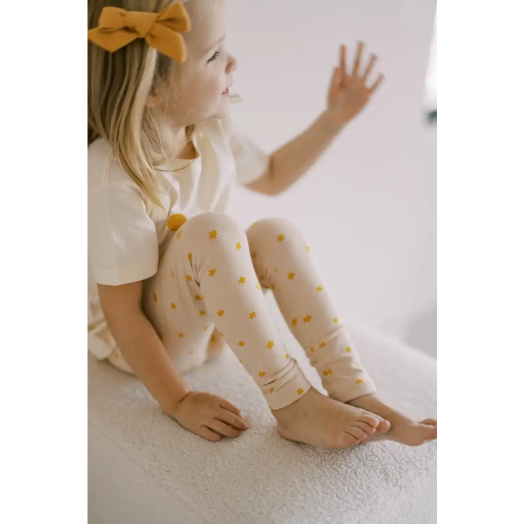 Child in white top and Bright Star leggings, rocking yellow polka dots and a bow