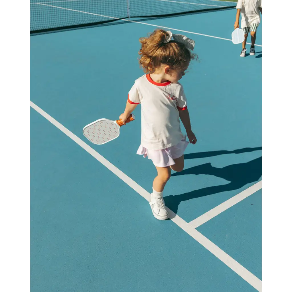 Young tennis player in white outfit with racquet wearing Soft Girls Club Ringer Tee