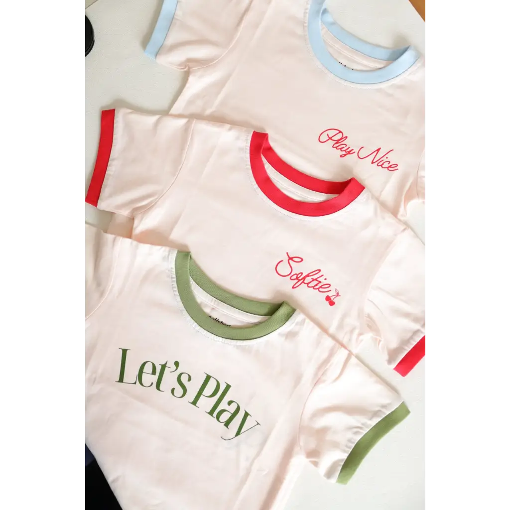 Three white Soft Girls Club Ringer Tees for kids with colorful trim and fun designs