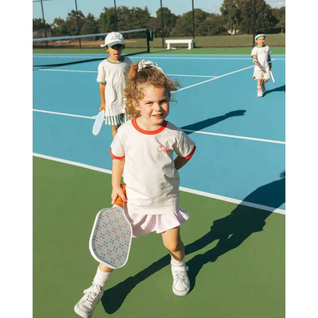 Young tennis player in white outfit showing off the Soft Girls Club Kids Ringer Tee