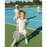 Young tennis player in white outfit showing off the Soft Girls Club Kids Ringer Tee