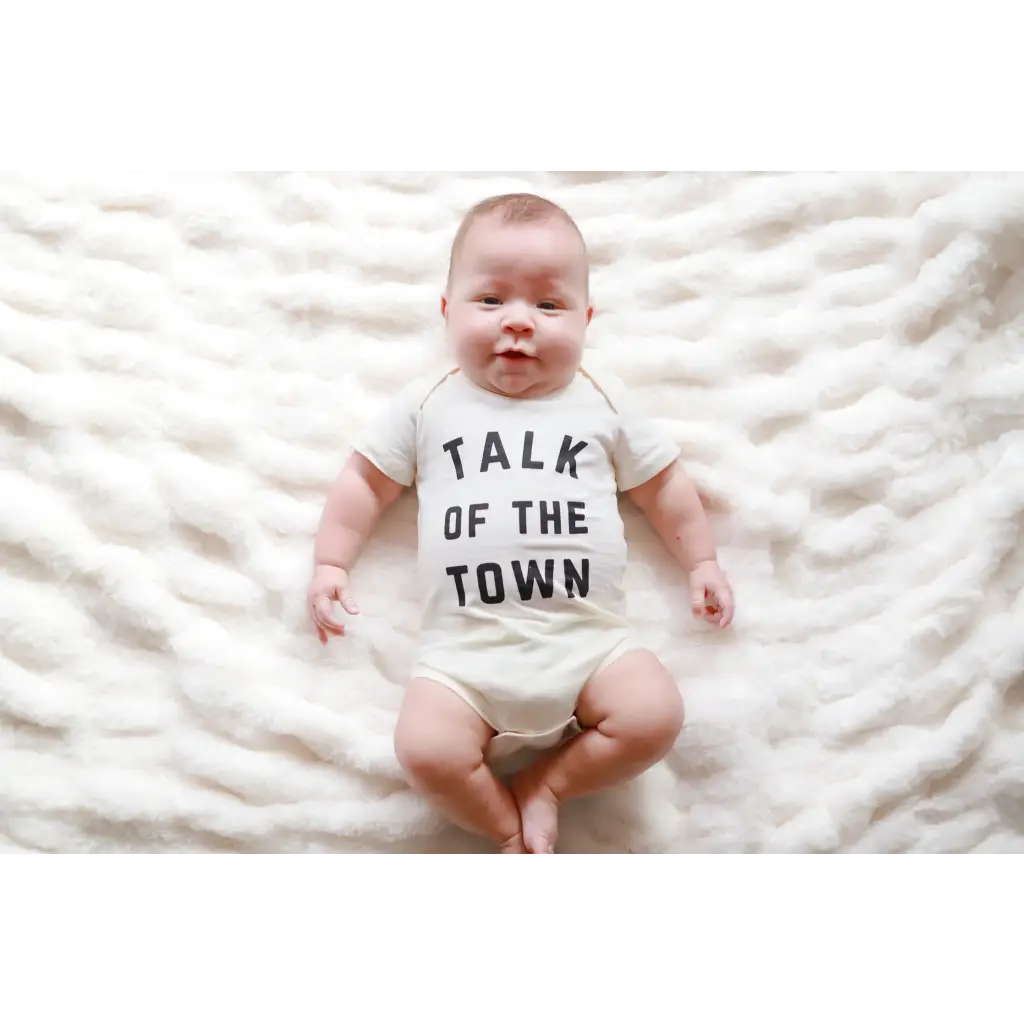 Baby in a white onesie saying TALK OF THE TOWN, made of soft organic cotton