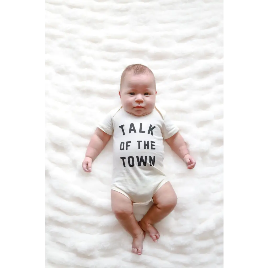 Baby in a white organic cotton onesie saying Talk of the Town for stylish newborns