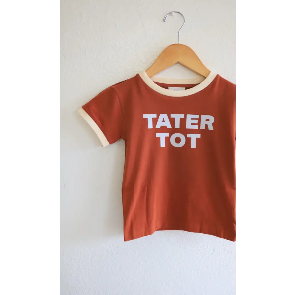 Rust t-shirt for tot kids with TATER TOT print and cream trim on a wooden hanger