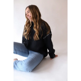 Person in a black Brandi Contrast Sweater and jeans laughing on the floor