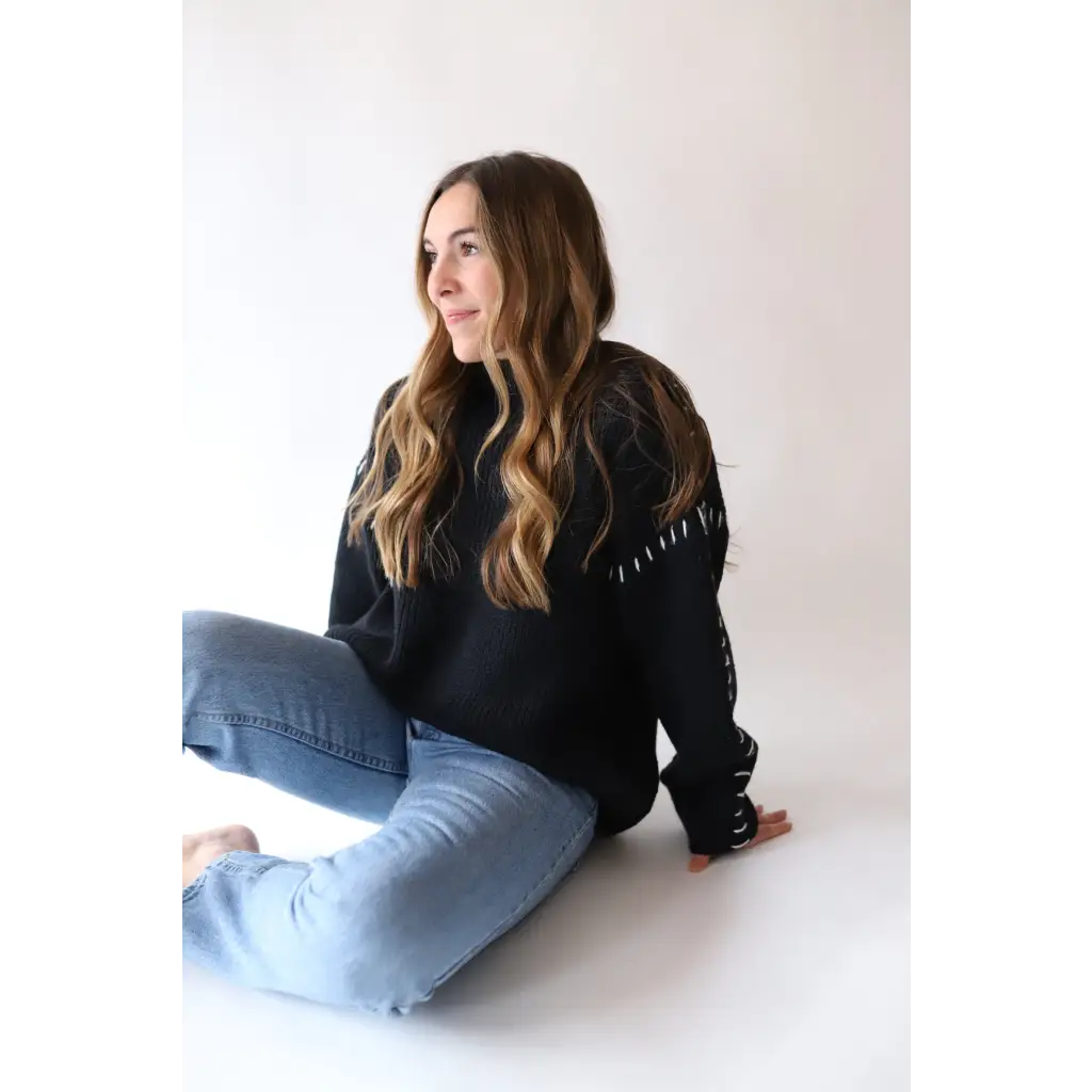 Person in a black Brandi Contrast Sweater and light blue jeans sitting on the floor