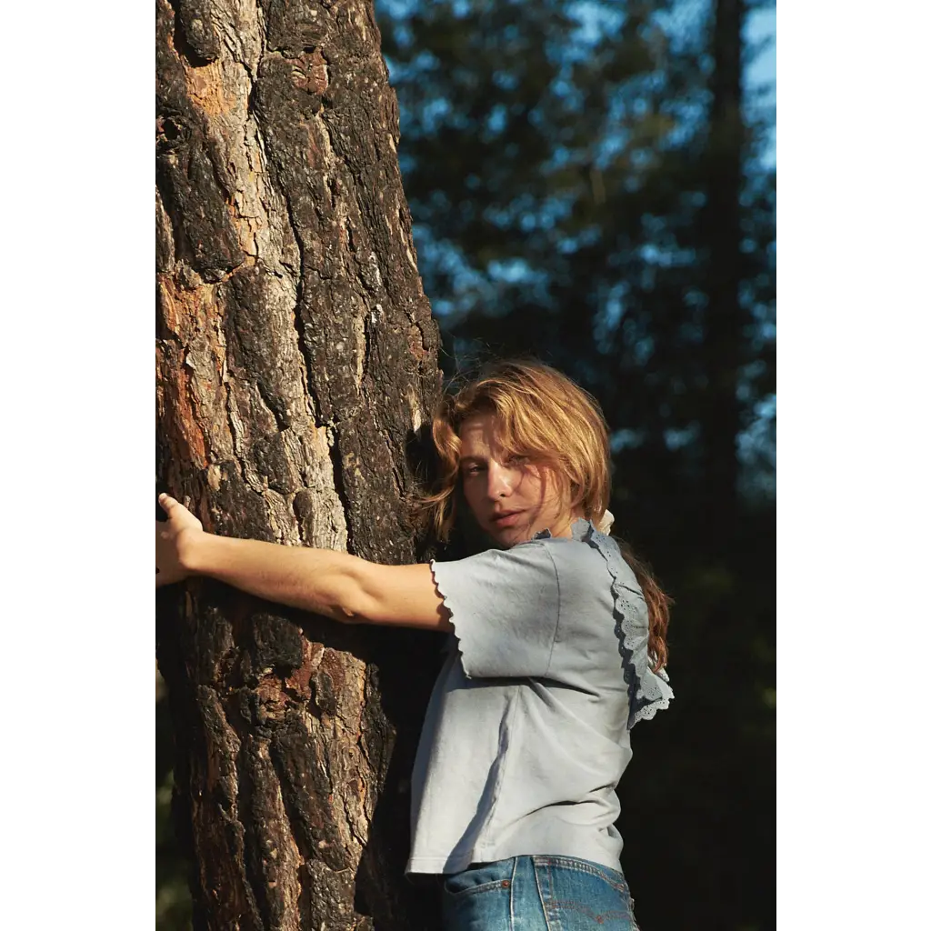 Woman in cottage tee leans on tree in stylish womens clothes