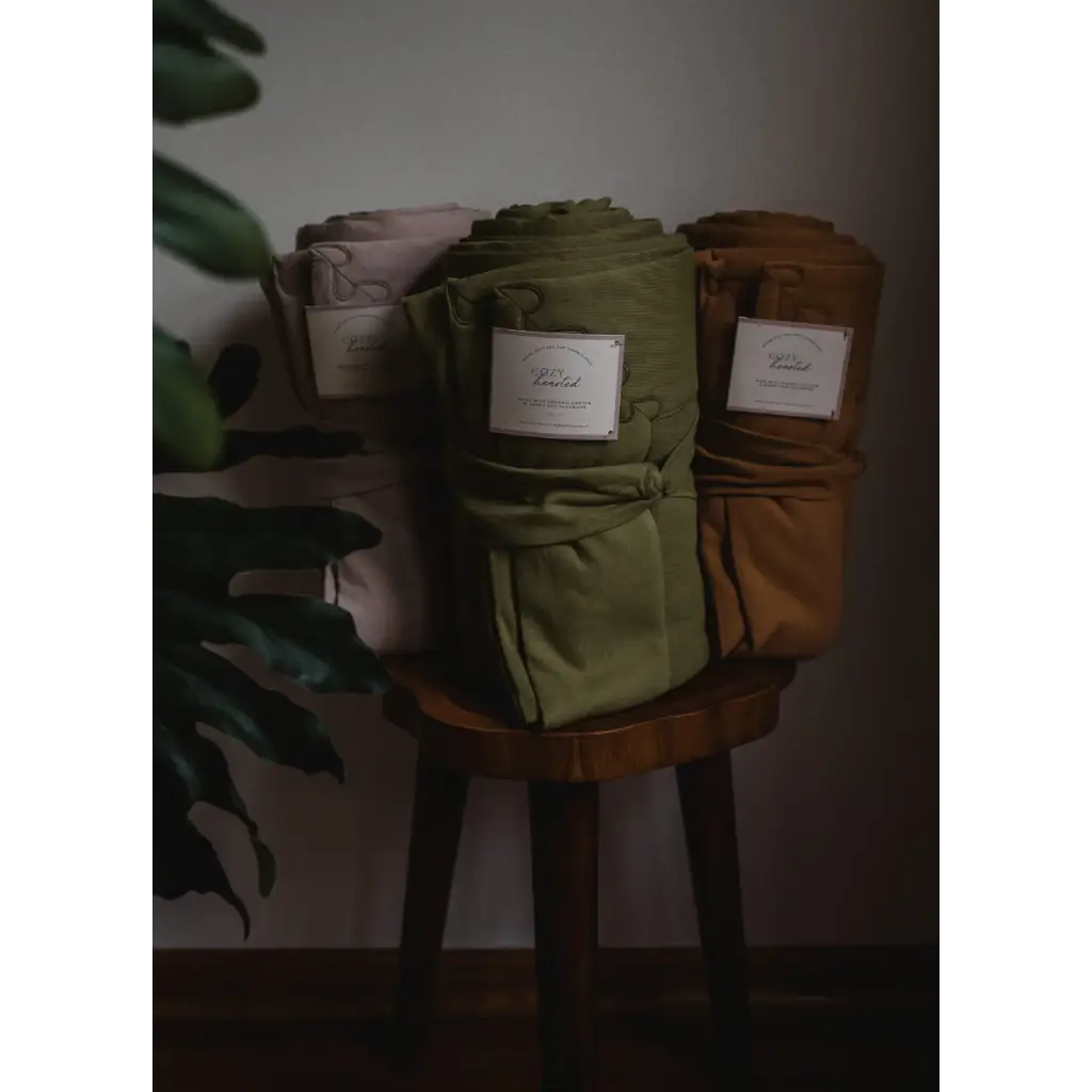 Three stylish fabric storage containers in pink, green, and brown next to an Organic Cotton Blanket