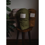 Three stylish fabric storage containers in pink, green, and brown next to an Organic Cotton Blanket