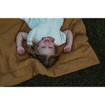 Person relaxing on a tan Organic Cotton Blanket in a light blue dress for ultimate comfort