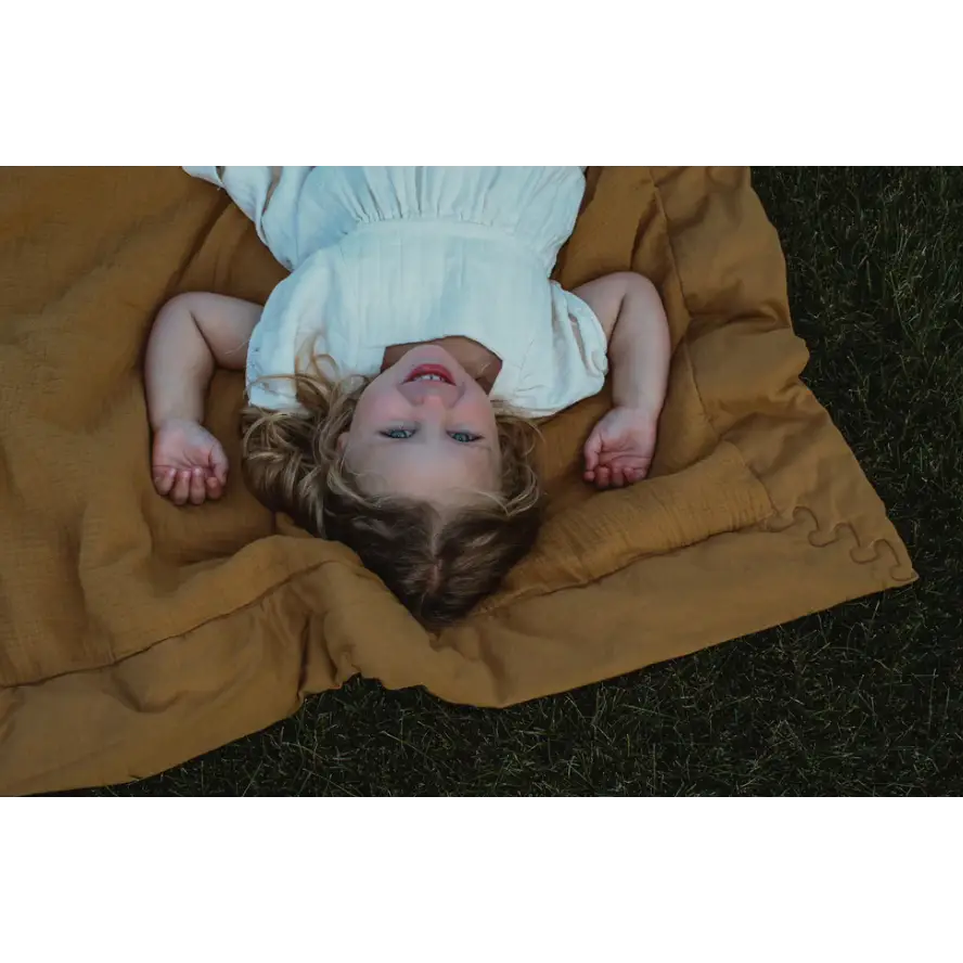 Person relaxing on a tan Organic Cotton Blanket in a light blue dress for ultimate comfort