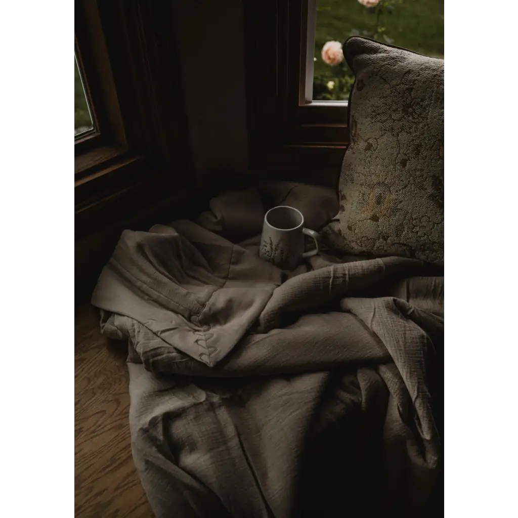 Rumpled gray blanket and coffee mug next to Cozy Premium Organic Cotton Blanket in Tan