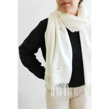 Cream-colored essential wool blend scarf with fringe over a black sweater