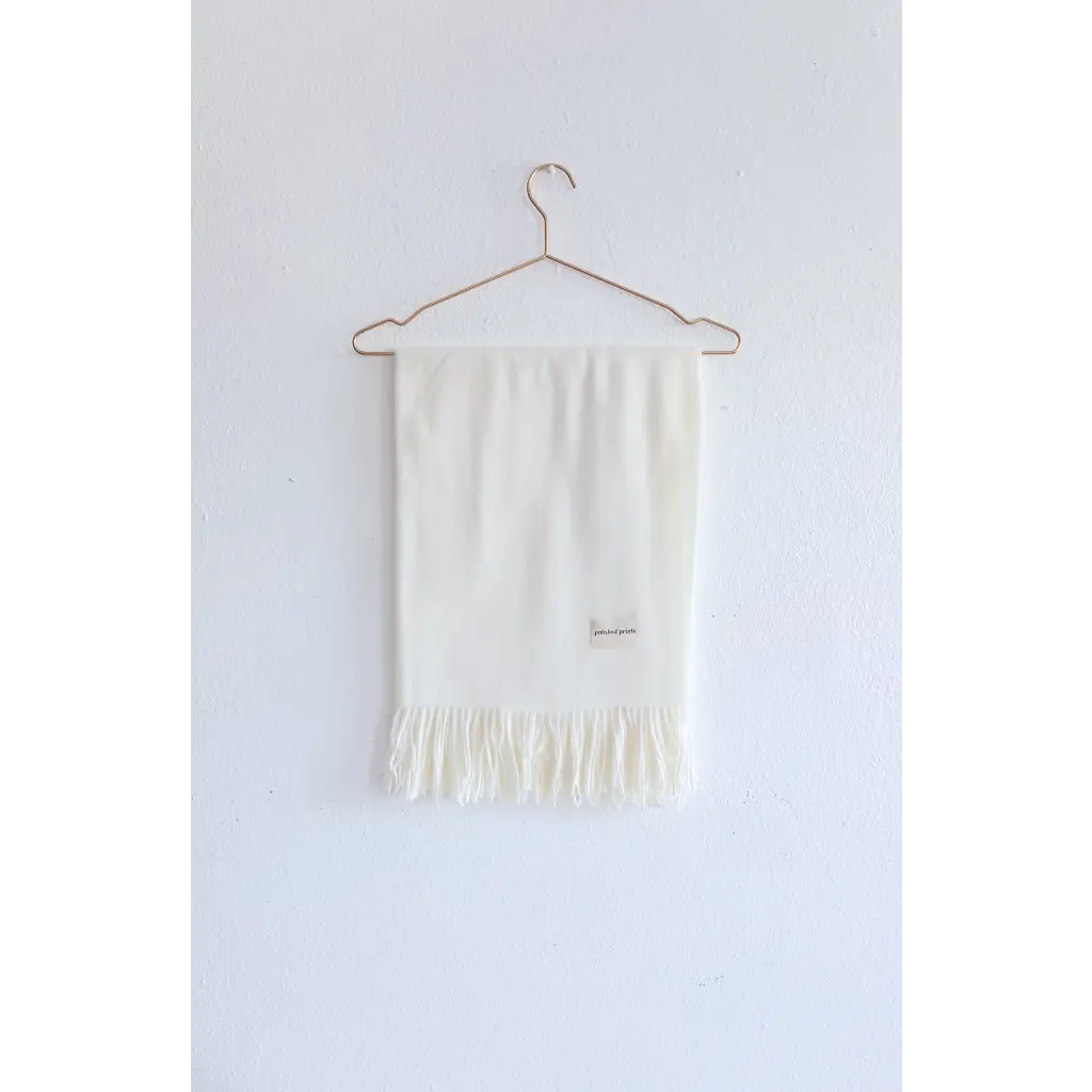 White fringed Essential Wool Blend Scarf hanging on a wire hanger in cozy neutrals