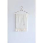 White fringed Essential Wool Blend Scarf hanging on a wire hanger in cozy neutrals