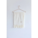 White fringed Essential Wool Blend Scarf hanging on a wire hanger in cozy neutrals