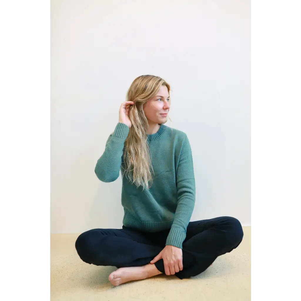 Blonde woman in teal Margo Crew Neck Sweater, sitting cross-legged and cozy