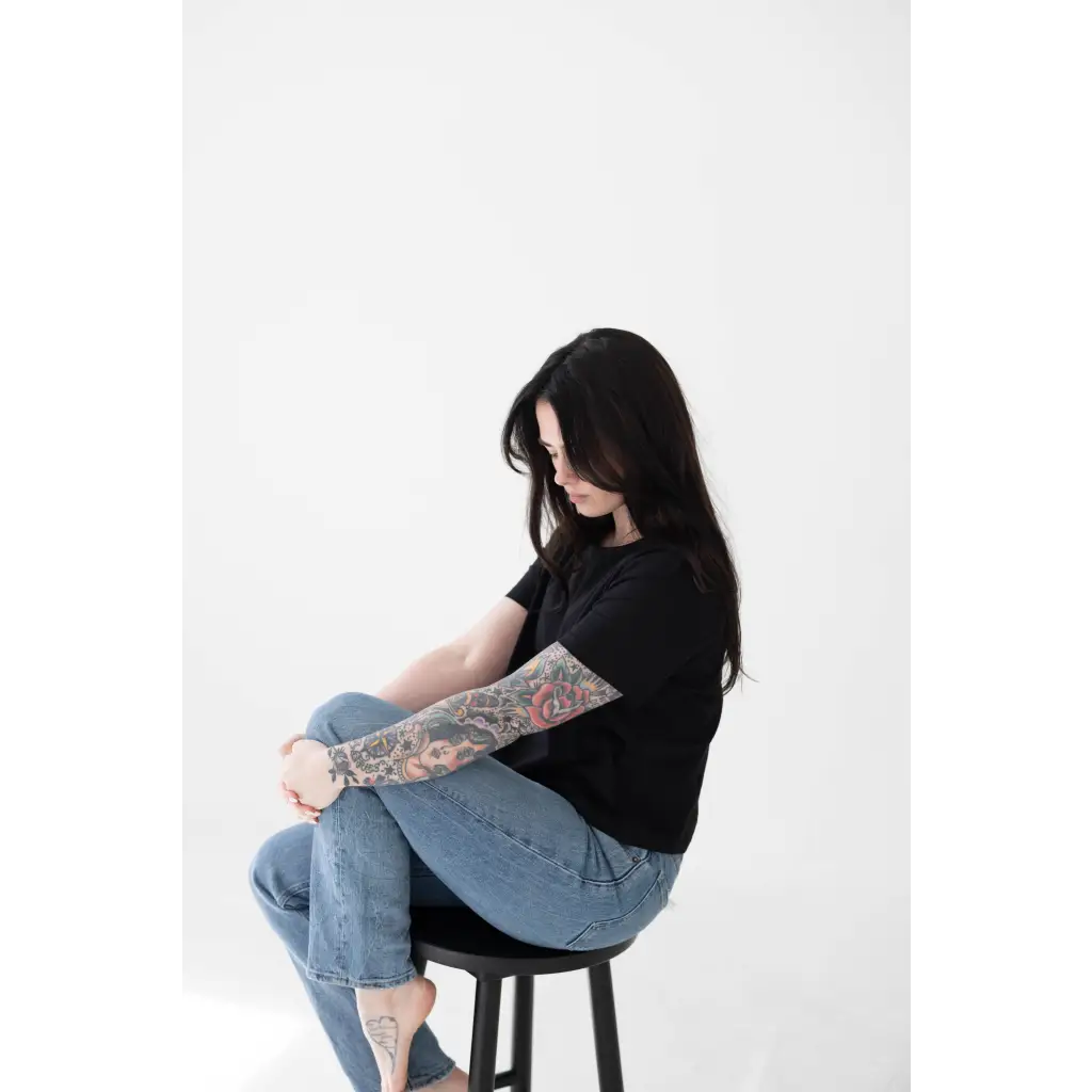 Person with dark hair in a black Stylish Mom Crop Boxy Tee sitting on a stool