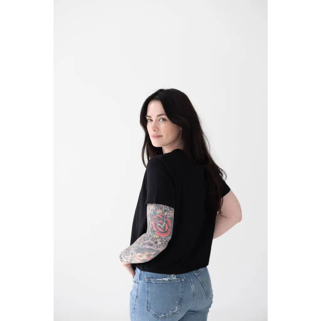 Person in a black mom crop boxy tee showing off a colorful sleeve tattoo