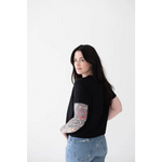 Person in a black mom crop boxy tee showing off a colorful sleeve tattoo