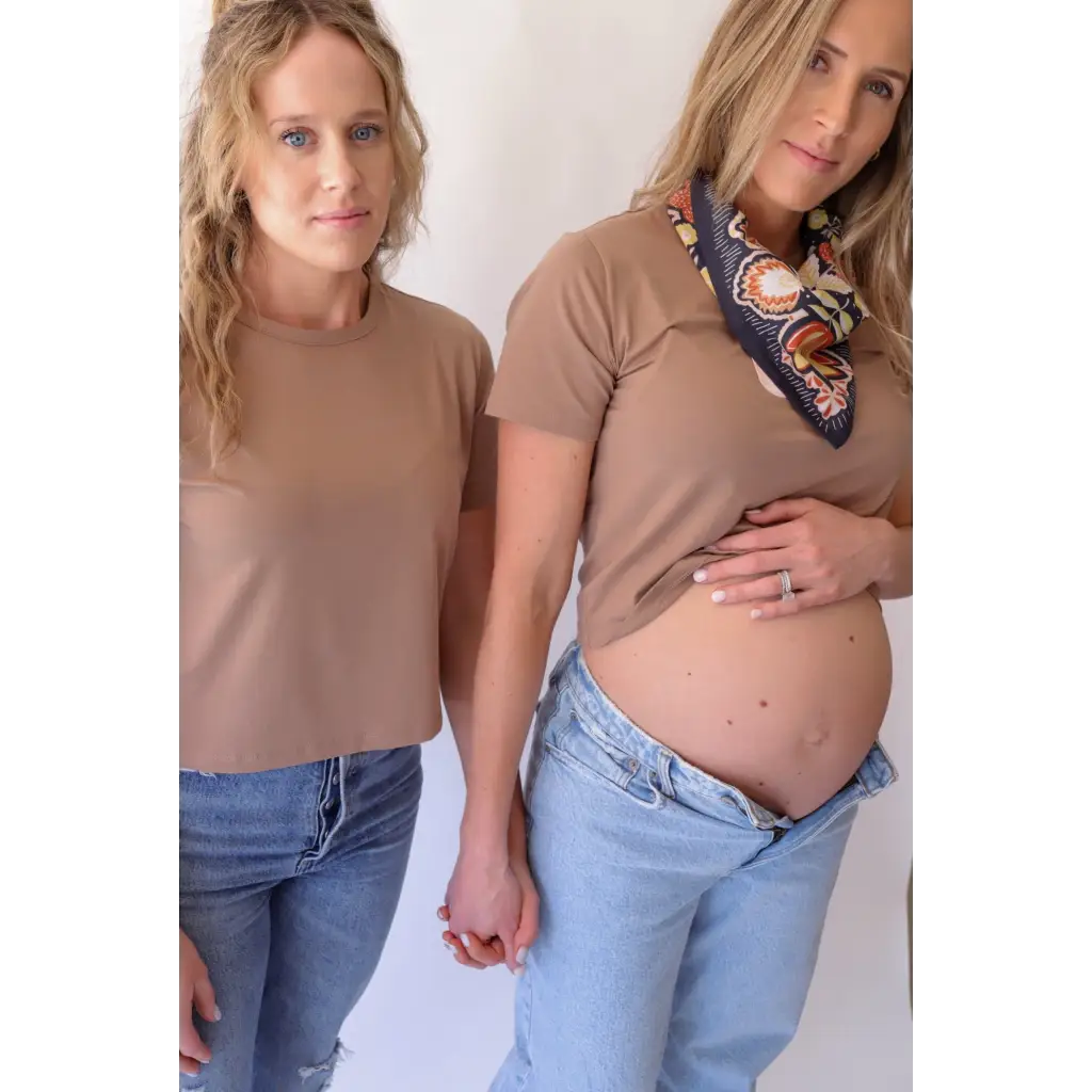 Two women in matching mom crop shirts and jeans, one pregnant, showcasing stylish womens clothes