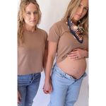 Two women in matching mom crop shirts and jeans, one pregnant, showcasing stylish womens clothes