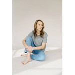 Person in a grey mom crop boxy tee and blue jeans sitting cross-legged on the floor