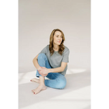 Person in a grey mom crop boxy tee and blue jeans sitting cross-legged on the floor