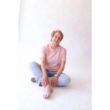 Older woman in pink shirt and jeans sitting cross-legged in The Mom Crop with polished prints