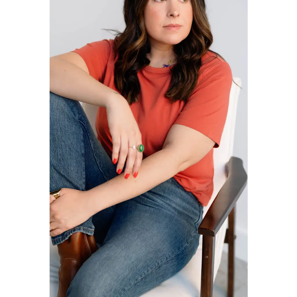 Person in a coral boxy tee designed for comfort, sitting in a chair with jeans