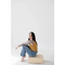 Person in a mustard yellow mom tank and blue jeans on a beige block, stylish womens clothes