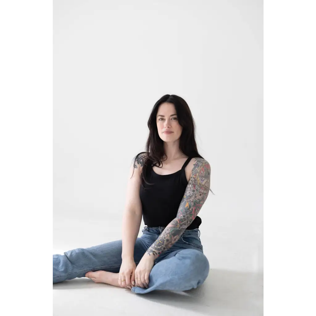 Person in a jet black mom tank and blue jeans, showing off polished prints and tattoos