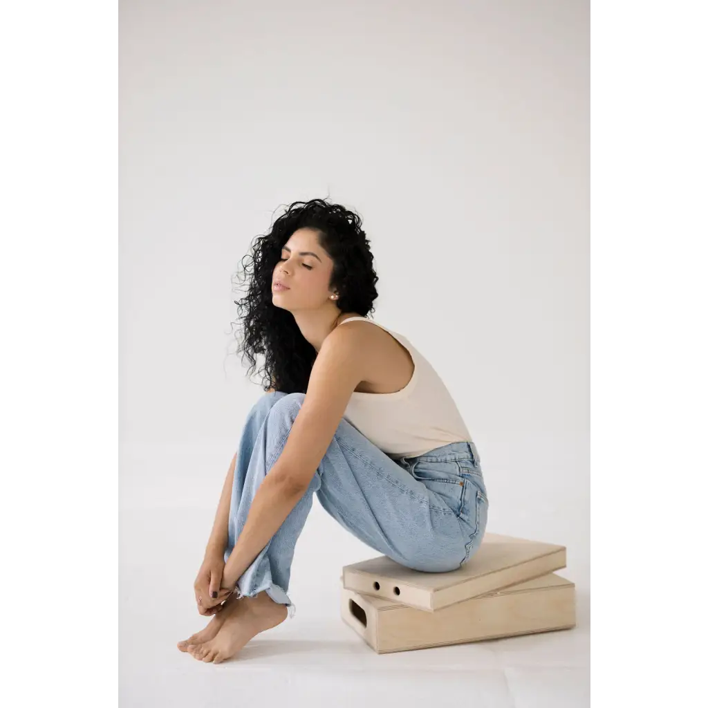 Person with curly dark hair in a white transitional tank and jeans, showcasing mom tank style