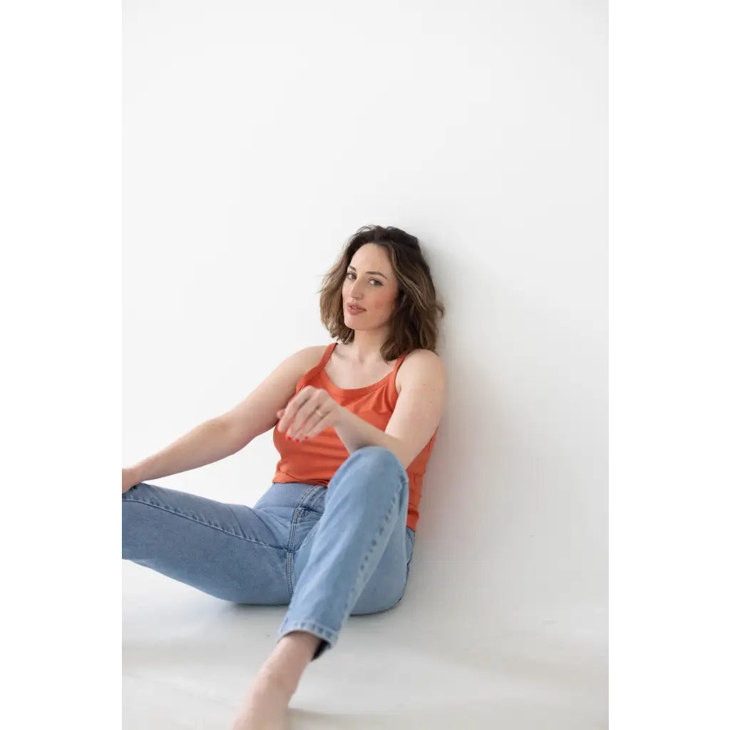 Woman in coral mom tank and light blue jeans, rocking polished prints against wall