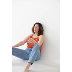 Woman in coral mom tank and light blue jeans, rocking polished prints against wall