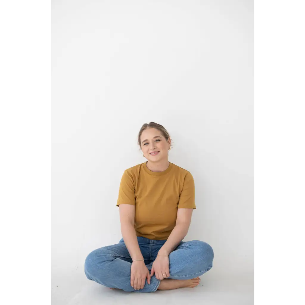 Person in a mustard yellow Mom Tee made of organic cotton and spandex blend, sitting cross-legged