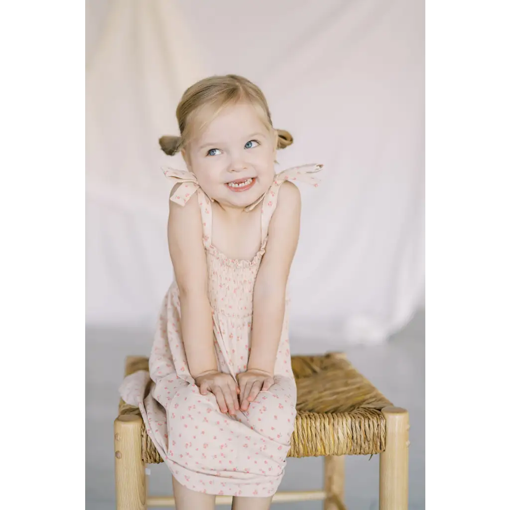 Child in a cute pale pink play dress sitting on a straw stool, perfect for summer fun