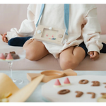 Baby in a white outfit with blue straps near cookies and Wakka Retro Water Game