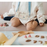 Baby in a white outfit with blue straps near cookies and Wakka Retro Water Game