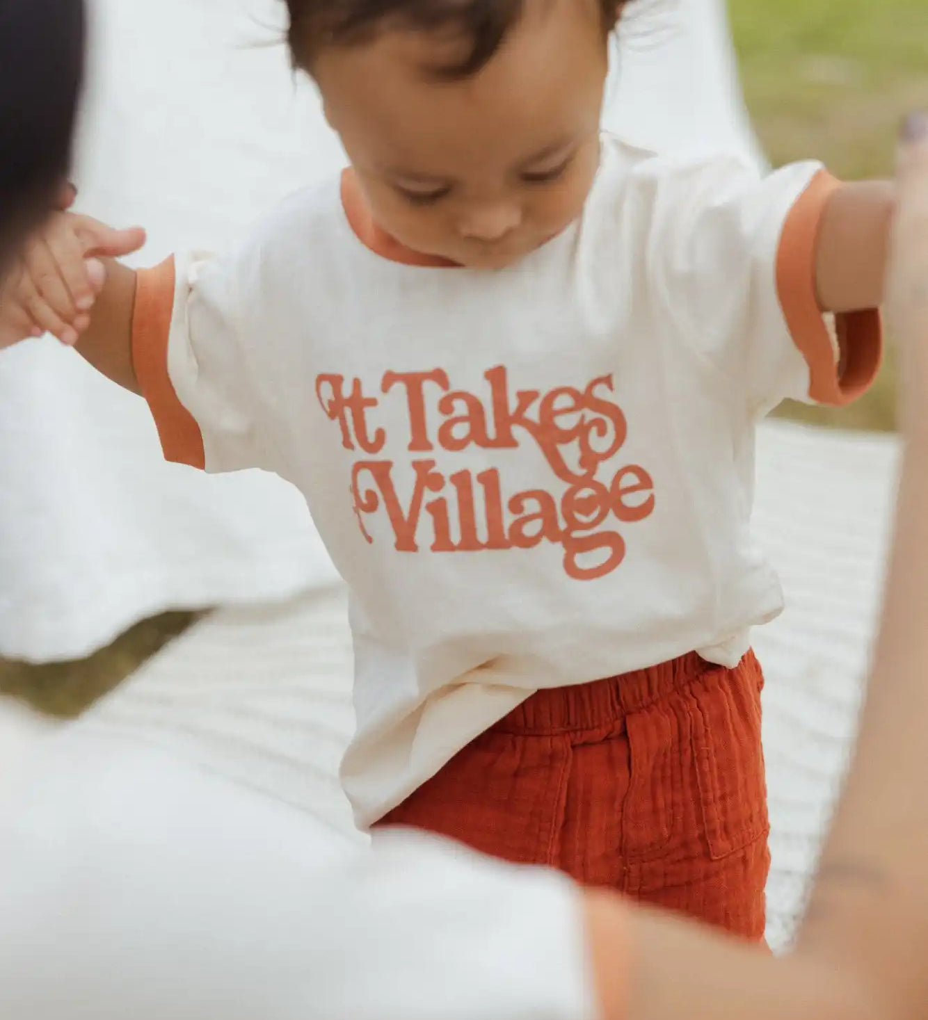 A white t-shirt with orange text reading ’It Takes a Village’