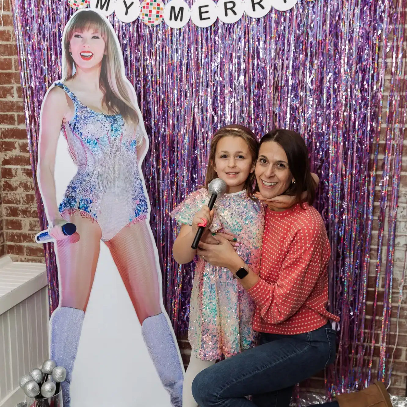 A woman and a young girl posing with a Taylor Swift cutout at a themed party.