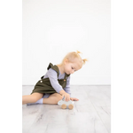Cute olive green kids overall dress with white trim beside wooden bunny push toy