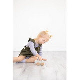 Cute olive green kids overall dress with white trim beside wooden bunny push toy